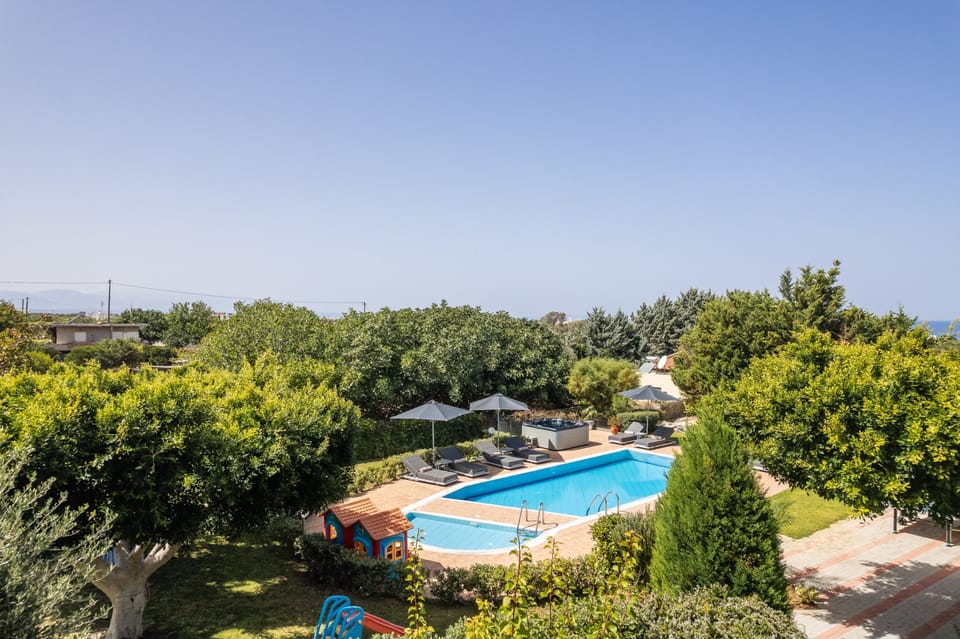 Outdoor area , surrounded by trees and flowers, with a pool & playground