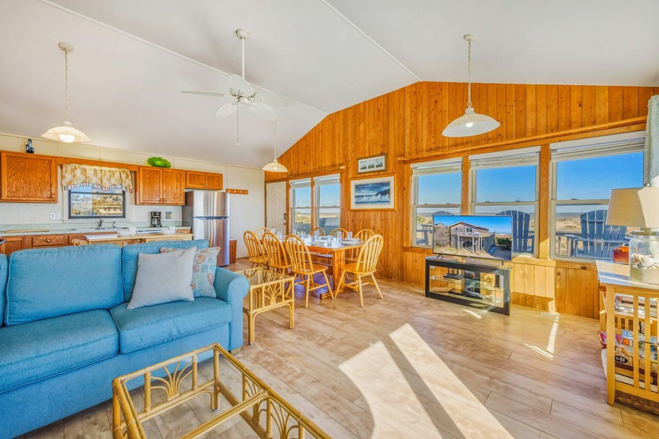 Relax in this open-plan living space where warm wood tones create a cozy coastal atmosphere, with panoramic ocean views through expansive windows.