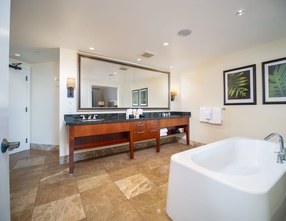 Indulge in relaxation with this spa-like bathroom featuring a deep soaking tub, double vanity, and natural stone flooring, offering a serene retreat during your Maui stay.