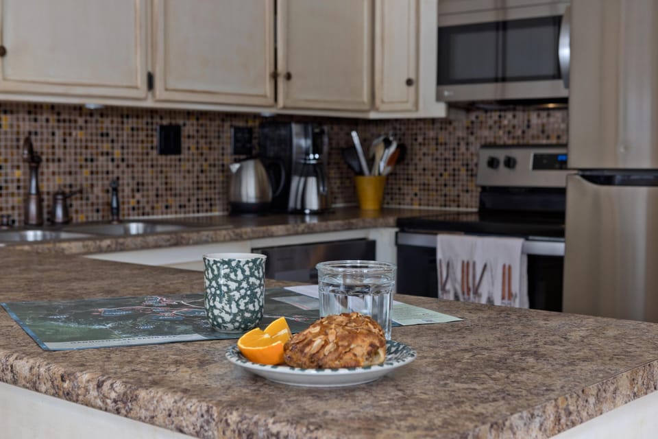 Polished stone counters wrap the breakfast bar, complemented by jewel-toned glass tilework behind premium cookware.