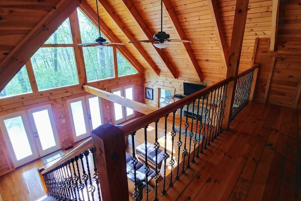 Upstairs loft overlooking the living room, featuring exposed wooden beams throughout the cabin — adding charm and a rustic, open feel.