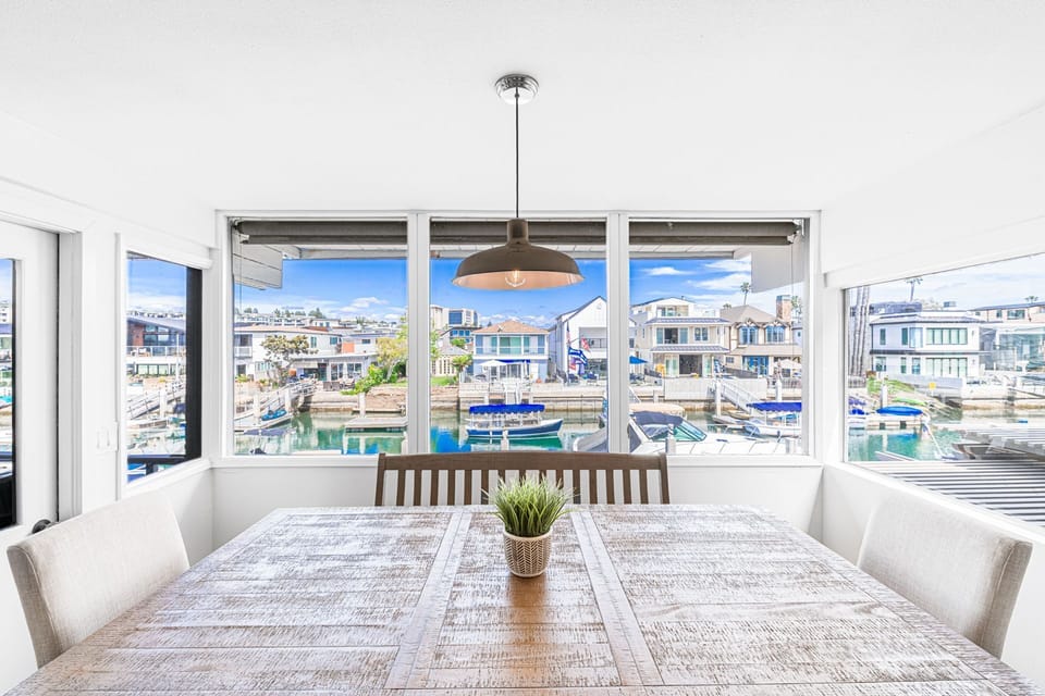 Sunlit dining area with wraparound windows showcasing beautiful bay views.
                