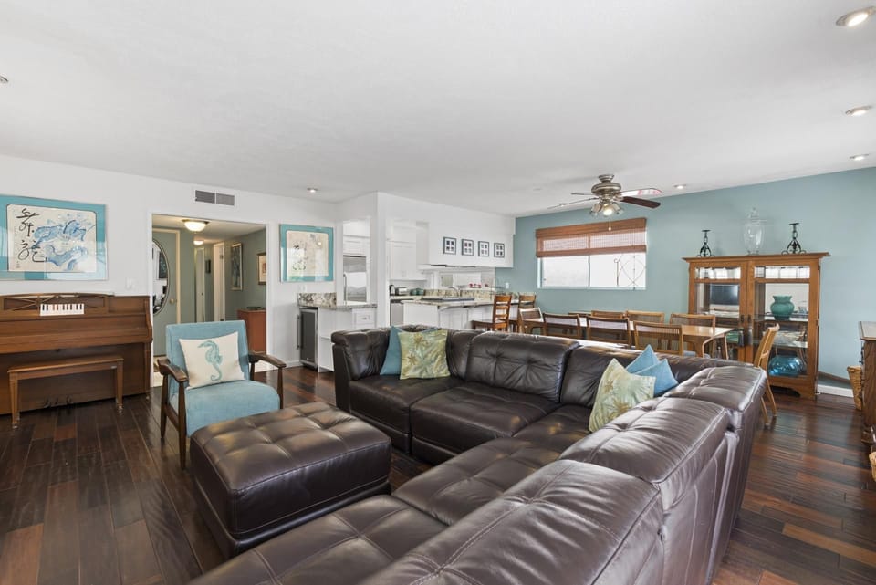 The main living area includes a leather sectional sofa, upright piano, cable TV, gas log fireplace, and dining table with seating for 8.
                