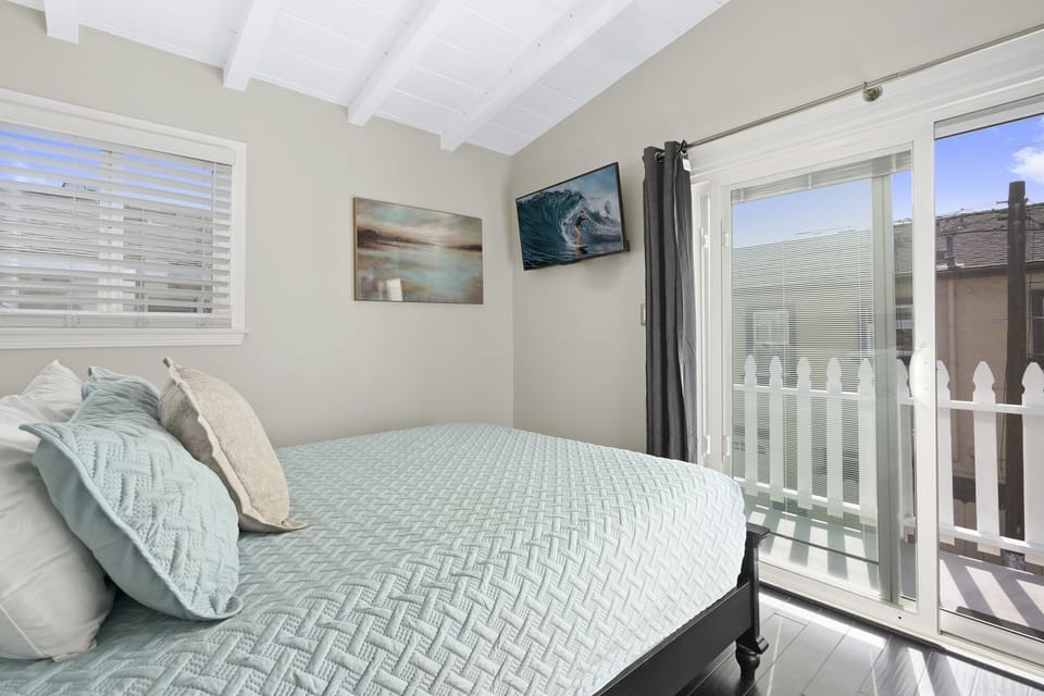 The primary bedroom is outfitted with a Queen bed, linens, TV, armoire, sliding glass doors out to private rear-facing balcony with seating.
                