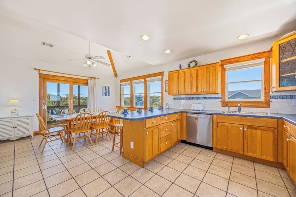 Gather in this sunlit kitchen and dining space, where warm wood cabinetry and spacious countertops invite you to cook memorable meals together, while multiple windows frame scenic views.