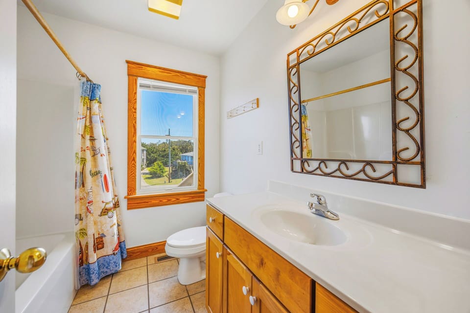 Your bathroom features a charming blend of classic and cozy touches, from the ornate mirror to the wood-framed window that invites natural light into the space.