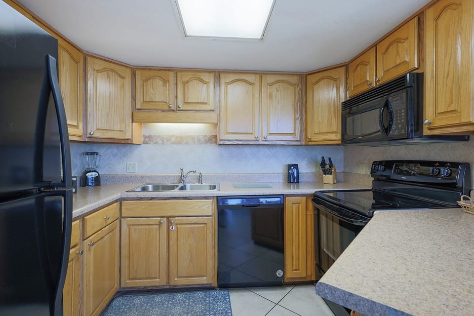 The kitchen features wooden cabinetry, a black refrigerator, and a sleek countertop with essential appliances for meal prep