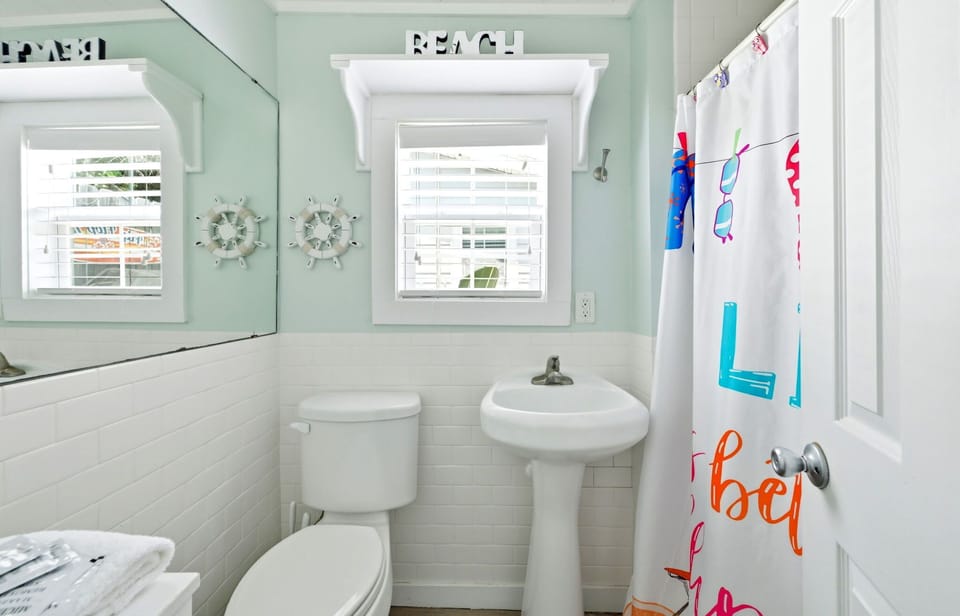 Bright bathroom with a pedestal sink, toilet, and playful coastal decor.