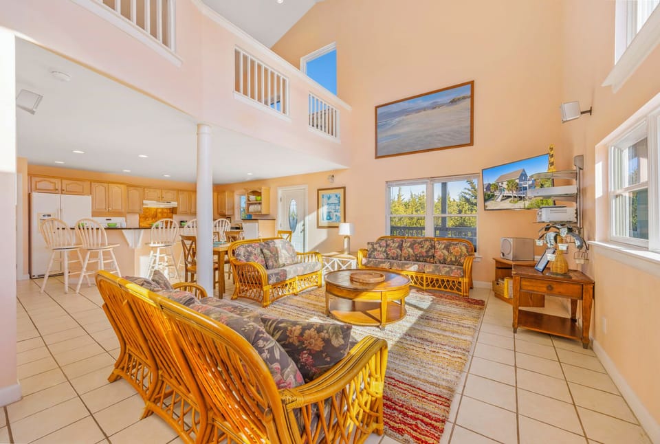 Relax in your spacious open-concept living area with tropical furnishings, soaring ceilings, and abundant natural light streaming through large windows.