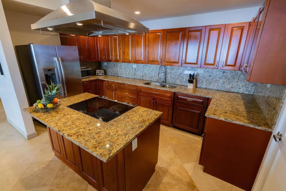 Granite countertops and backsplash complement cherry wood cabinetry around the kitchen’s center island with electric cooktop.