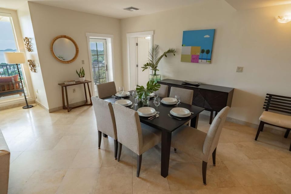 A dark wood dining table set for six contrasts with beige upholstered chairs and light tile flooring.