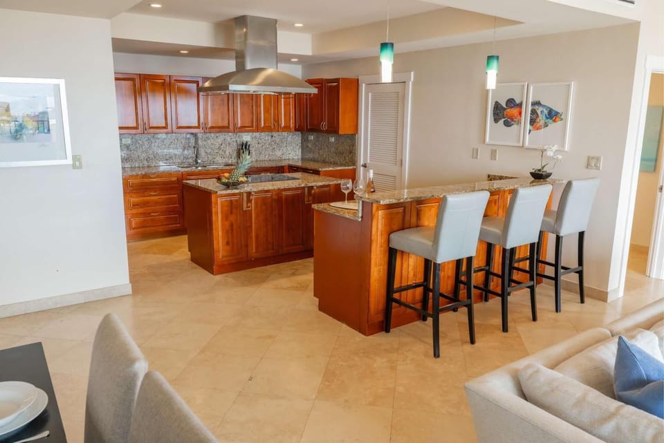 Granite countertops top the kitchen island and breakfast bar with three gray leather stools beneath teal pendant lights.