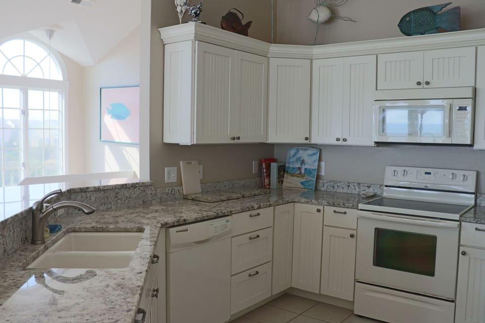 Your fully equipped kitchen features granite countertops and coastal decor, perfect for preparing meals with ocean views streaming through the window.