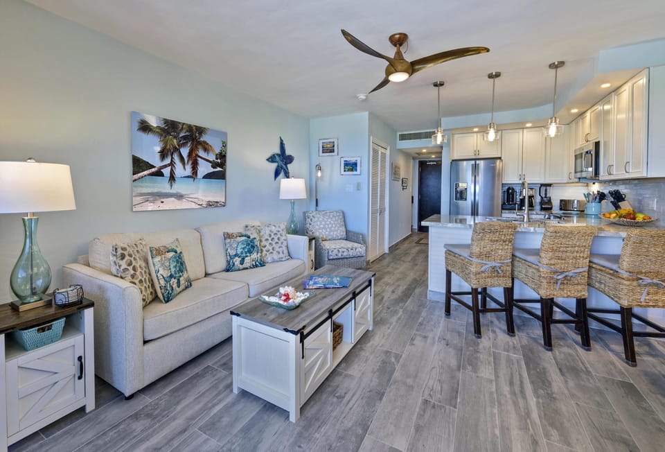 Open living area featuring new floors, new sofa sleeper, woven bar stools, and coastal wall art.