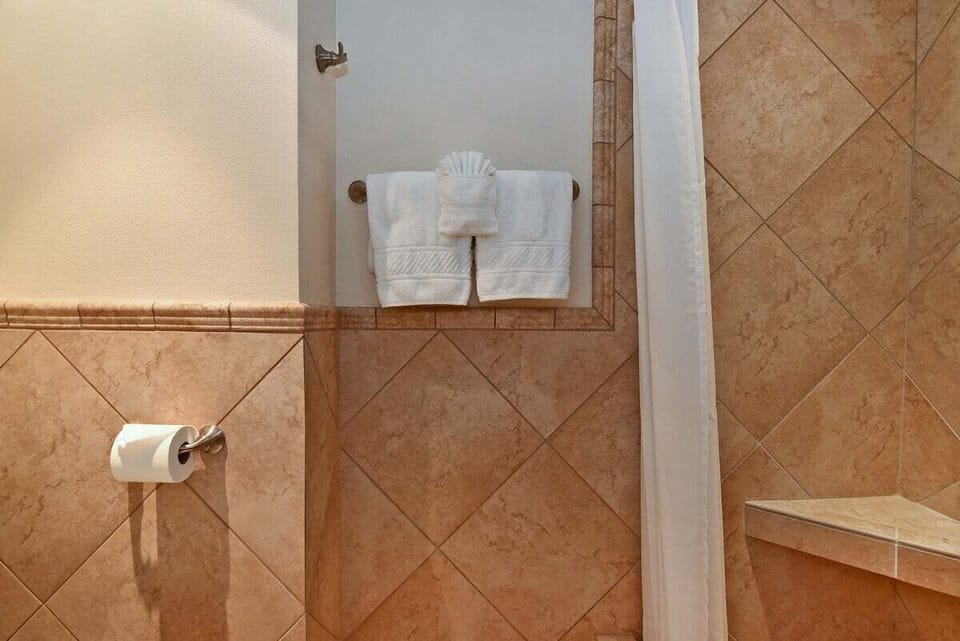 A pristine, tiled walk-in shower featuring classic earth-toned masonry and fresh, fluffy white towels ready for use.