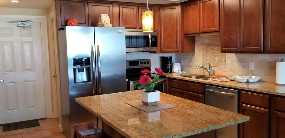 Granite countertop island with a floral centerpiece sits beneath a pendant light in the kitchen’s warm wood cabinetry.