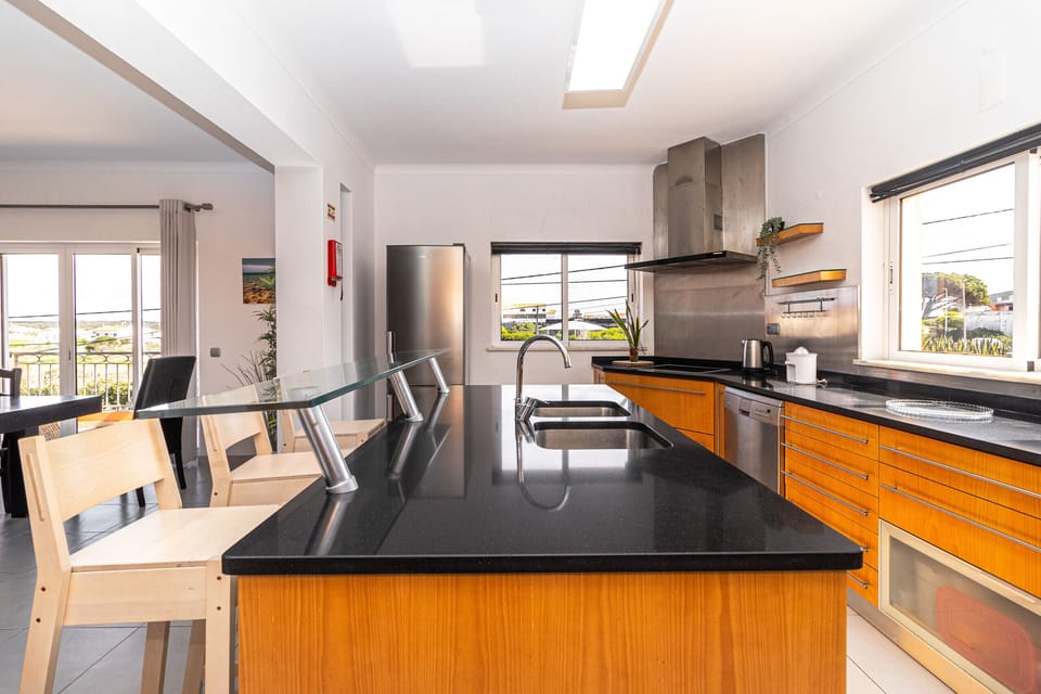 Modern open-plan kitchen and dining area with orange cabinetry and black countertops — Villa Farol, luxury holiday villa in Vila do Bispo