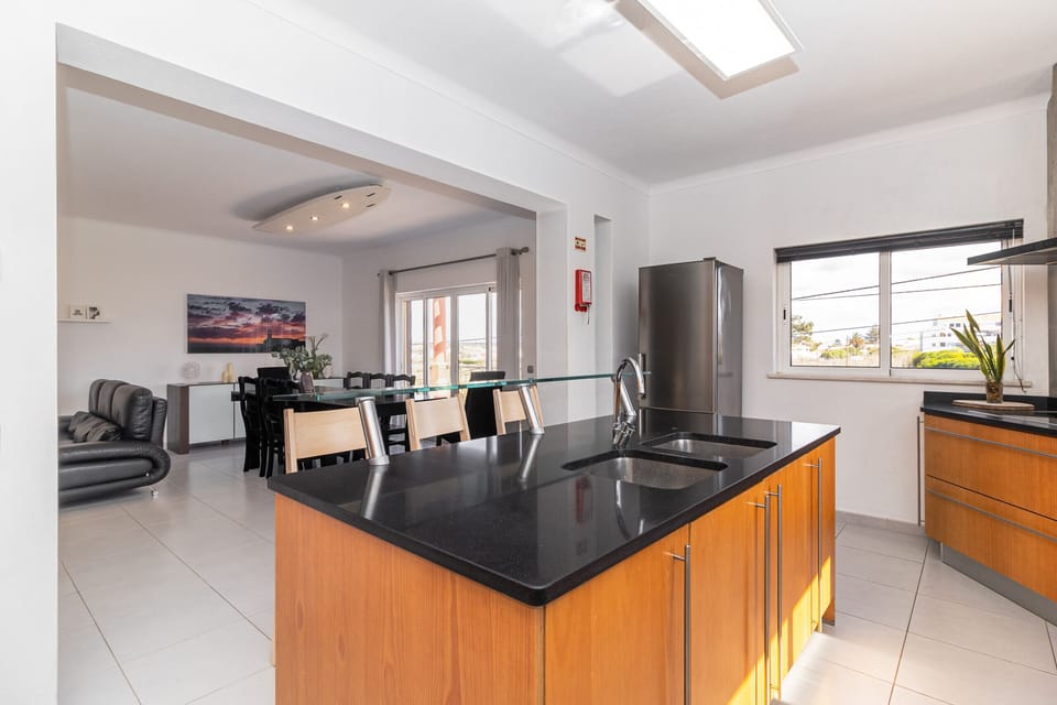 Modern open-plan kitchen with black granite island and wood cabinetry — Villa Farol, luxury holiday villa in Vila do Bispo