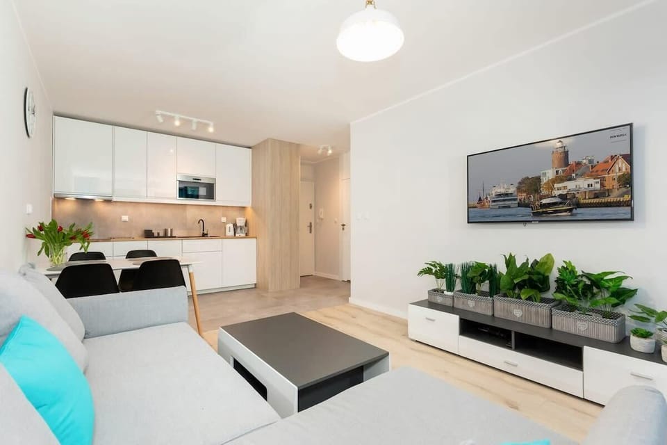 A cozy, open-plan living room with a sofa, wall-mounted TV, and decor in soft shades, with turquoise accents for added vibrancy.