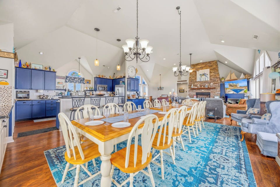 Gather everyone around this generous dining table under vaulted ceilings. The open layout lets you chat with the chef, share stories, and feel right at home in this inviting coastal space.