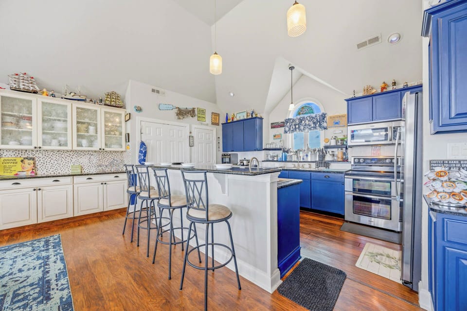 Gather around the spacious island in this bright, thoughtfully designed kitchen with charming coastal blue cabinetry, modern appliances, and warm wood floors—perfect for preparing meals together or sipping morning coffee.