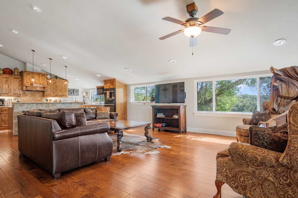 A cozy living room with leather sofas, a wooden coffee table, and a TV, seamlessly connects to a rustic kitchen.