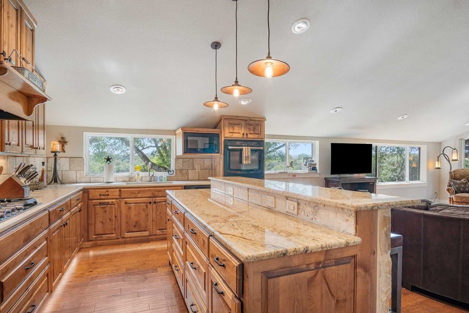 A well-appointed kitchen features light wood cabinetry, granite countertops, and a large island, with a view of the outdoors.