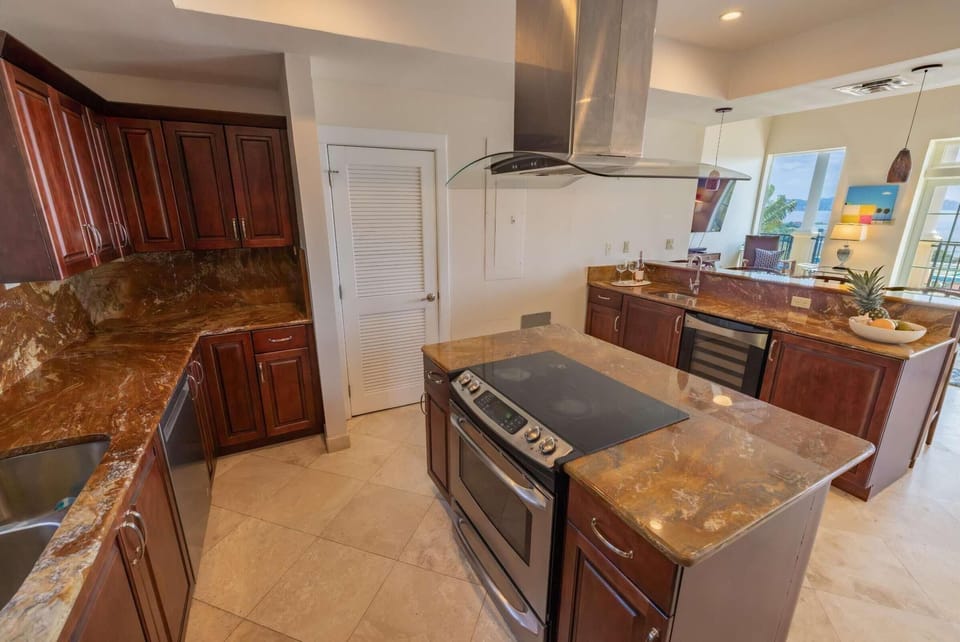 Brown marble countertops and cherry wood cabinetry surround the island cooktop in the kitchen.