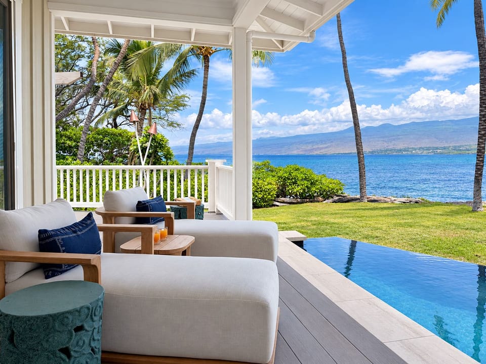The pool-edge lounge looks straight down the coastline, lawn running out past the deck.