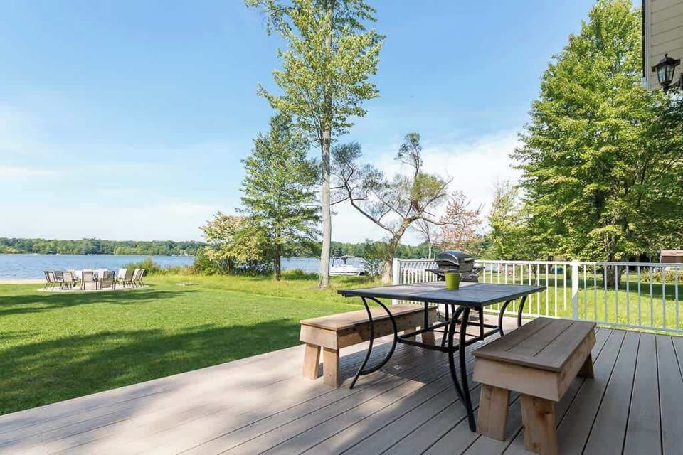 Lake-facing Sunset Shores Lake House deck with dining sets. NEW for spring 2024: XL Titan park-style charcoal grill!