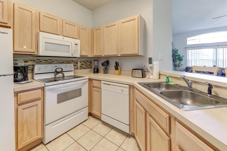 Double stainless steel sink sits beneath a broad counter, dividing the kitchen from the living area with vaulted ceilings.