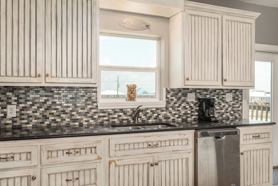 Your fully equipped kitchen features elegant white cabinetry, granite countertops, and mosaic tile backsplash - perfect for preparing meals during your stay.
