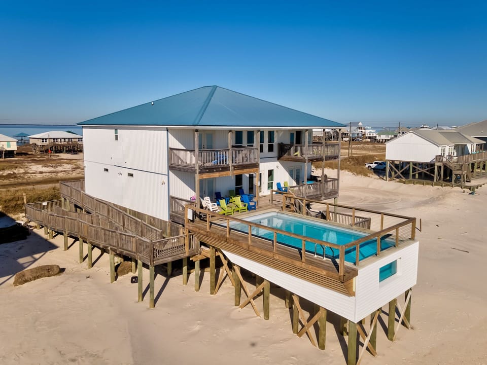 Elevated beachfront property featuring private pool and expansive deck overlooking sandy shores under clear blue skies.