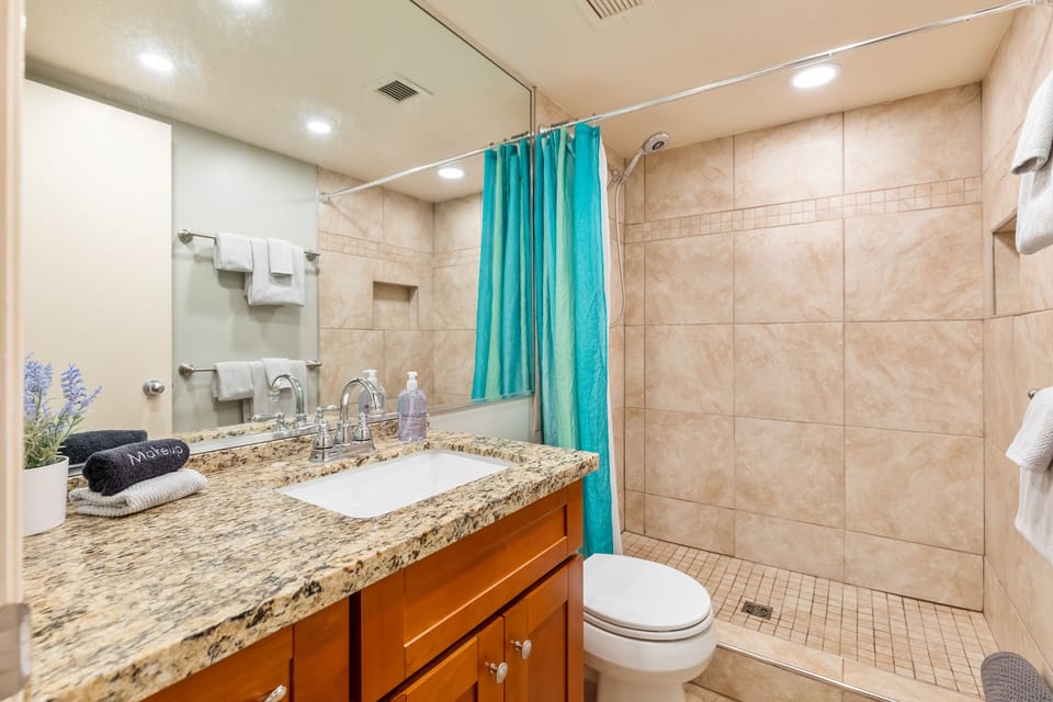 Bathroom off the kitchen with a tile shower and granite counter.