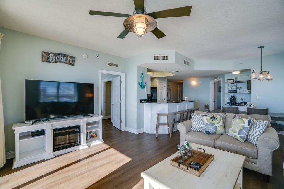 Relax in your coastal-themed living space with comfortable seating, modern entertainment center, and breezy ceiling fan overhead.