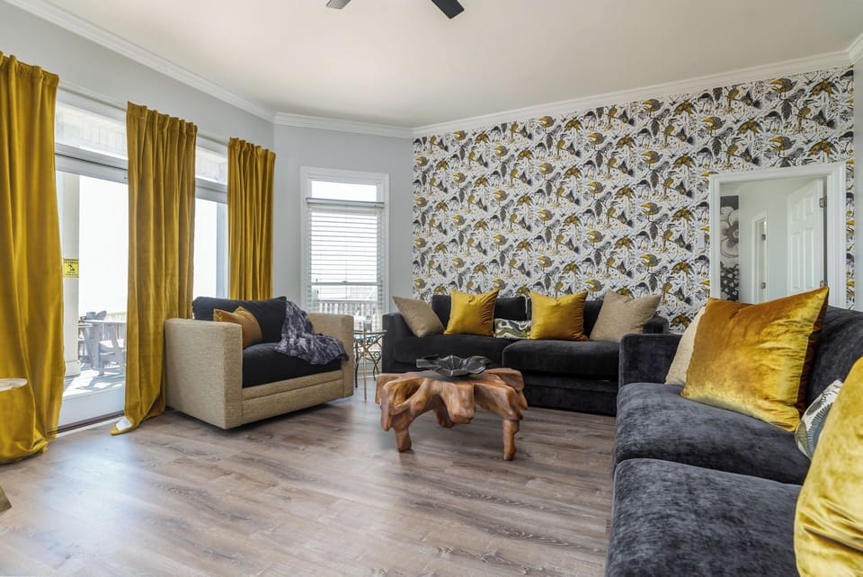 Sink into plush velvet seating with golden accents in this stylish living space, where bold wallpaper and natural light create your perfect retreat.