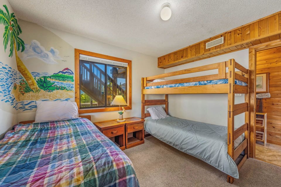 A cheerful beach mural adds tropical charm to this cozy sleeping space with warm wood paneling, featuring a bunk bed and twin bed, perfect for kids or groups seeking coastal comfort.