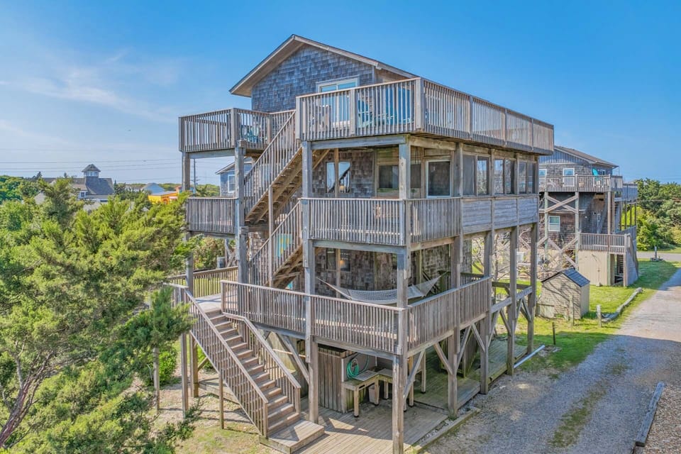 A weathered coastal home elevated on stilts sits amid lush greenery in a tranquil beachside neighborhood, offering a relaxed atmosphere for your stay.