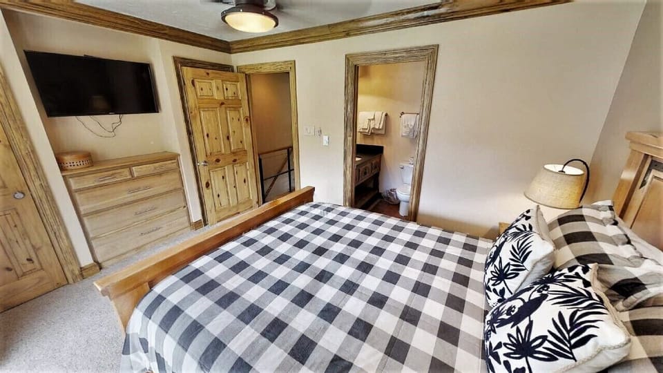 Slip into cozy comfort in this charming bedroom featuring rustic wood furnishings and a restful buffalo-check bedspread. Your private bathroom awaits just steps away through the en-suite door.