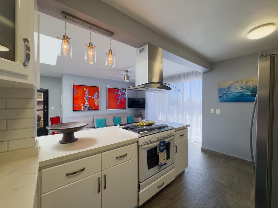 Kitchen with white cabinetry, marble countertops, stainless steel range hood, and pendant lighting above the island.