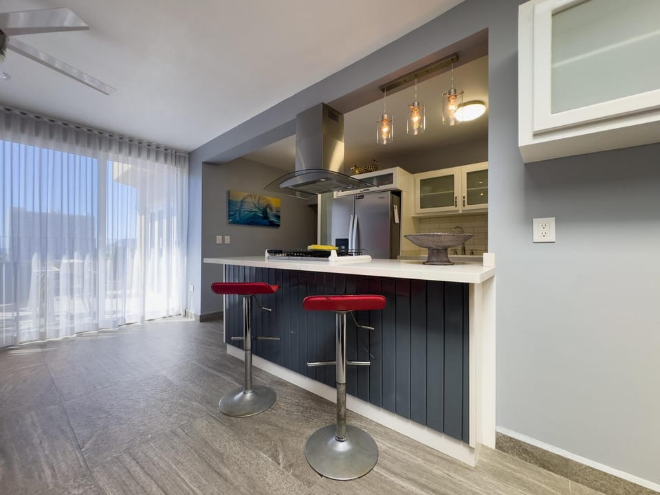 Kitchen island with black vertical paneling, white countertop, two red bar stools, and stainless steel range hood.
