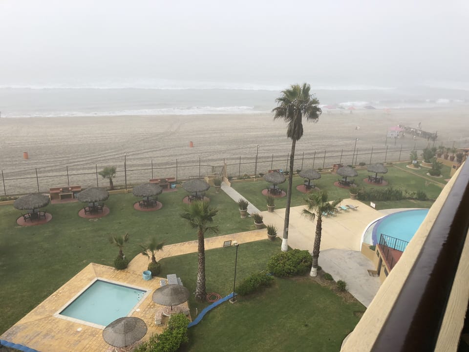 View from balcony of gated pool, grassy lounge area, playground and bbq 