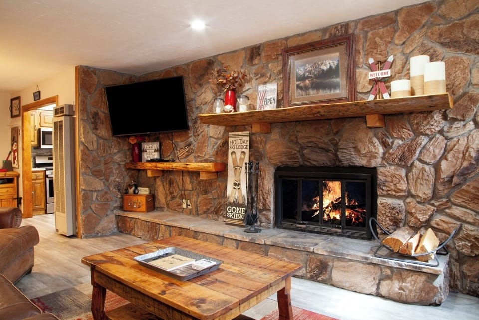 Unwind in your cozy living room, where a crackling stone fireplace and rustic wooden beams create the perfect mountain retreat ambiance.
