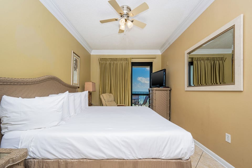 Inviting master bedroom features a king bed, a cozy armchair, and a view of the balcony with glimpses of the gulf beyond