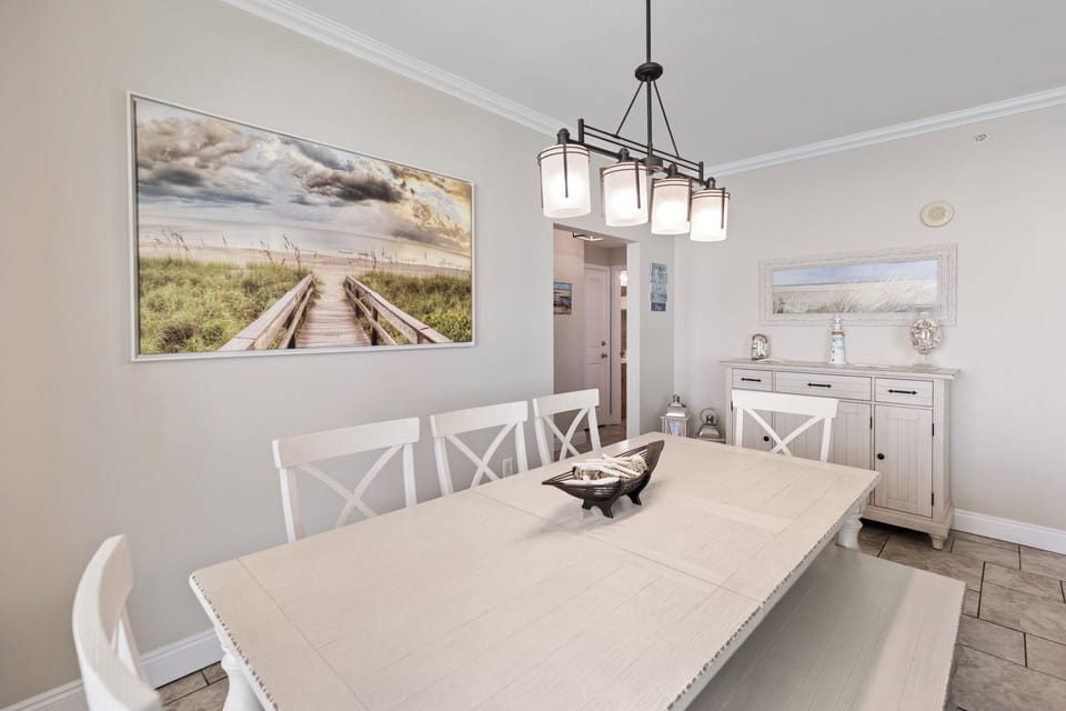 Gather around this elegant dining table where coastal artwork and warm lighting create the perfect atmosphere for memorable meals together.