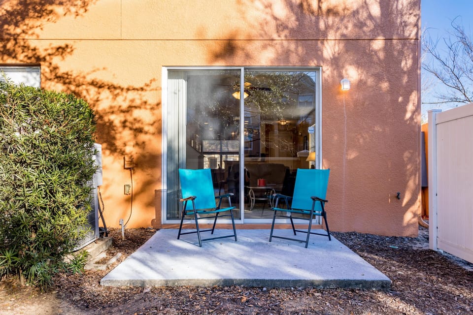Concrete patio with two turquoise metal chairs outside sliding glass doors on terracotta stucco wall.