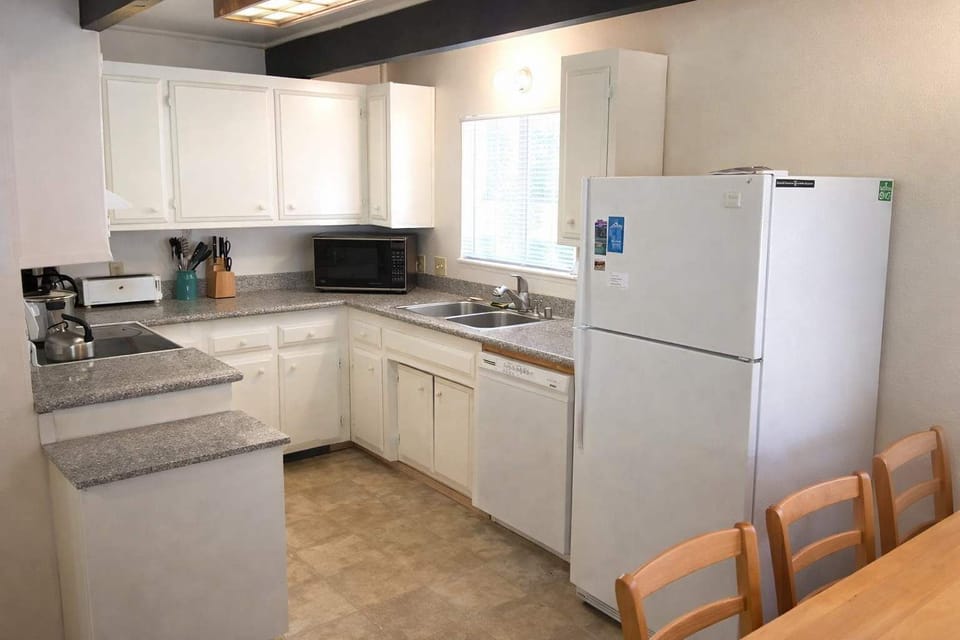 Bright, fully equipped kitchen with white cabinetry, full-size appliances, ample counter space, and dining table for easy meals.
