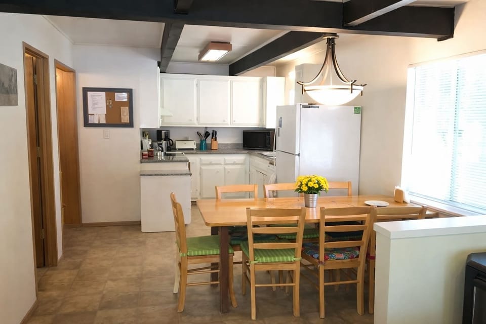 Bright open kitchen and dining area with wood table, white cabinetry, modern lighting, and plenty of space for shared meals.
