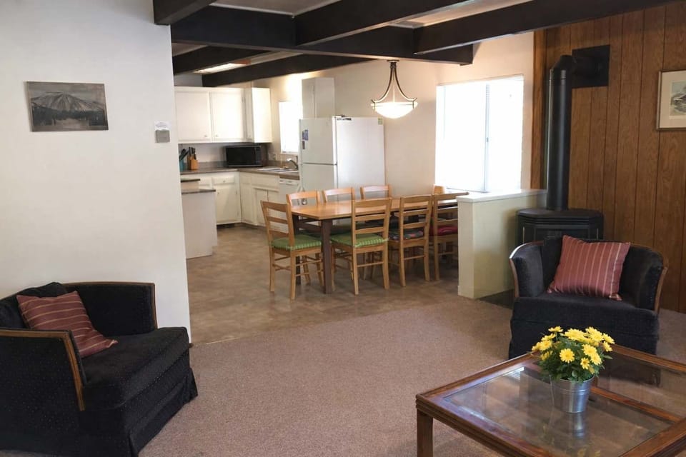 Spacious living area with cozy seating, coffee table, and open view to the dining space and kitchen, filled with natural light.
