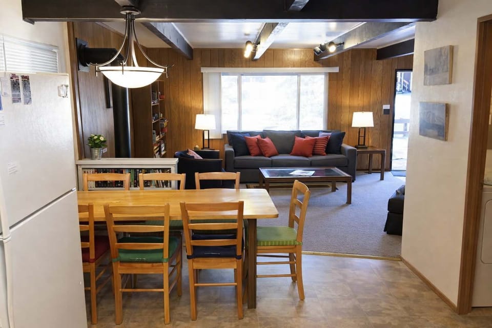Open-plan dining and living area with wood accents, dining table for gatherings, cozy sofa, and bright natural light—ideal for relaxing together.
